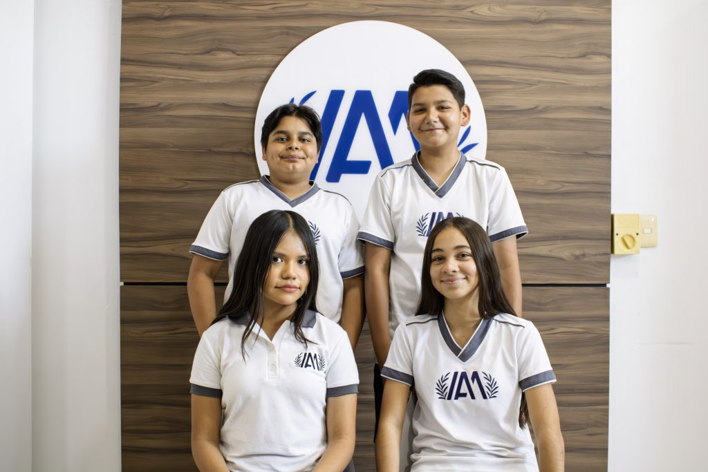 Cuatro alumnos de Secundaria con el uniforme del Instituto Anglo Moderno frente al logotipo del colegio
